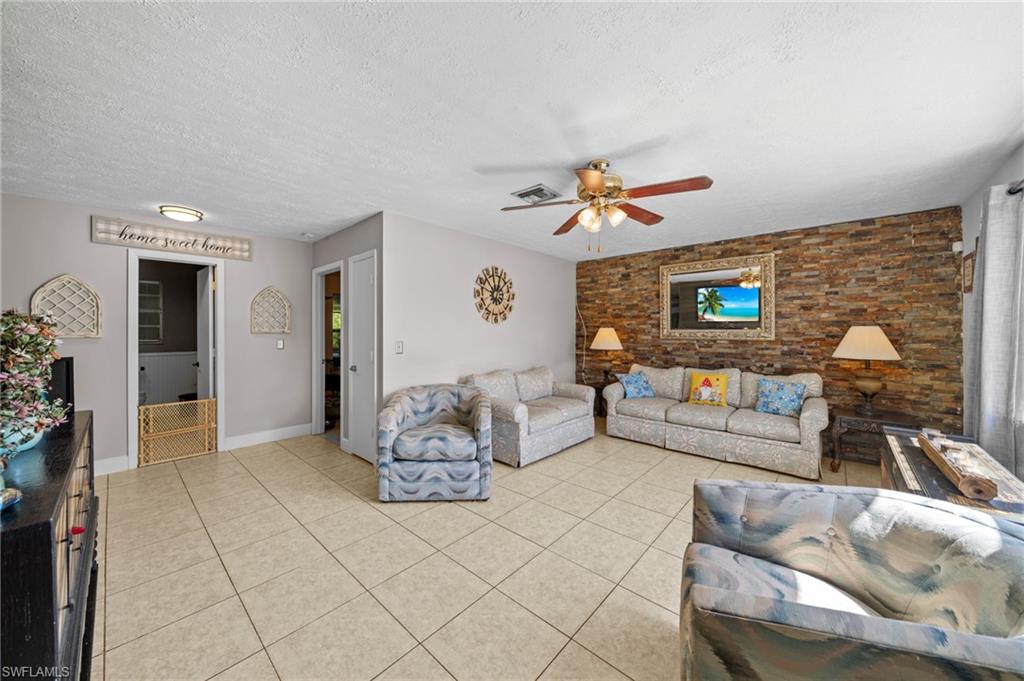 Living room featuring a textured ceiling, light tile patterned flooring, a ceiling fan, and an accent wall