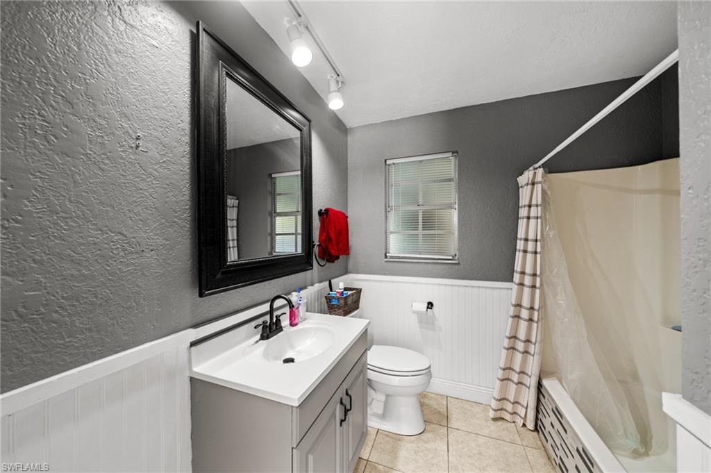 Full bathroom with a textured wall, shower / tub combo with curtain, baseboard heating, vanity, and wainscoting