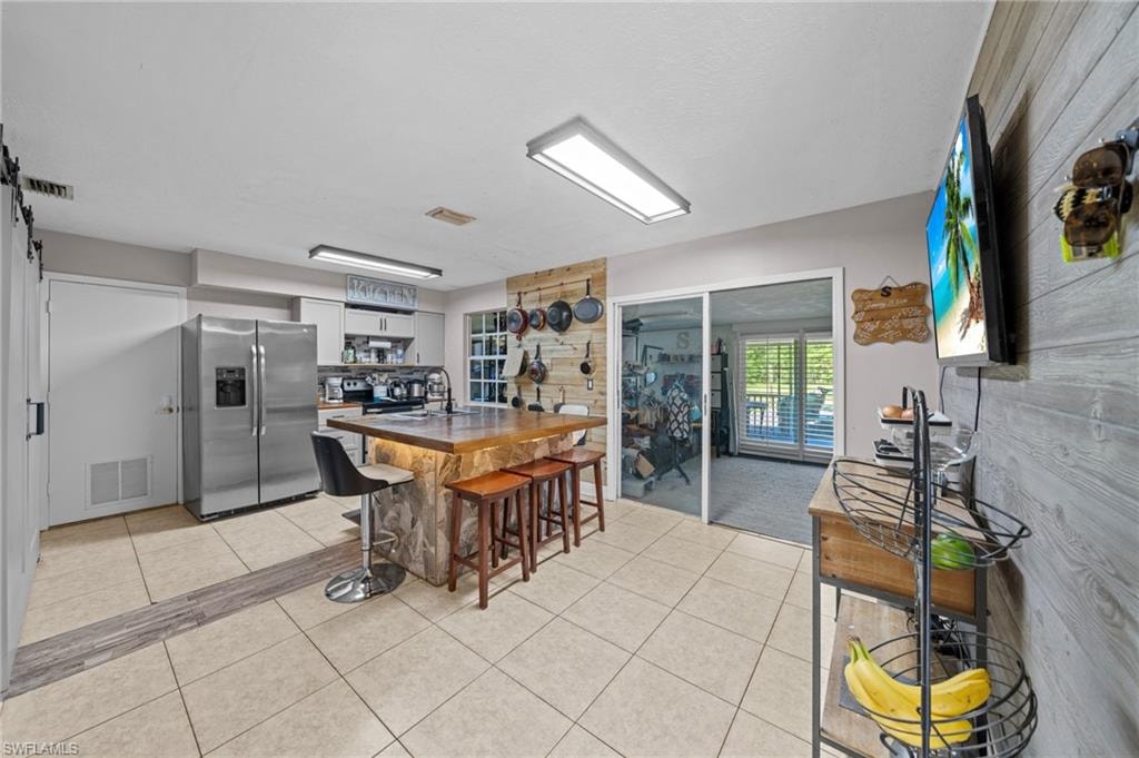 Kitchen featuring open shelves, a kitchen bar, stainless steel fridge, light tile patterned floors, and a barn door