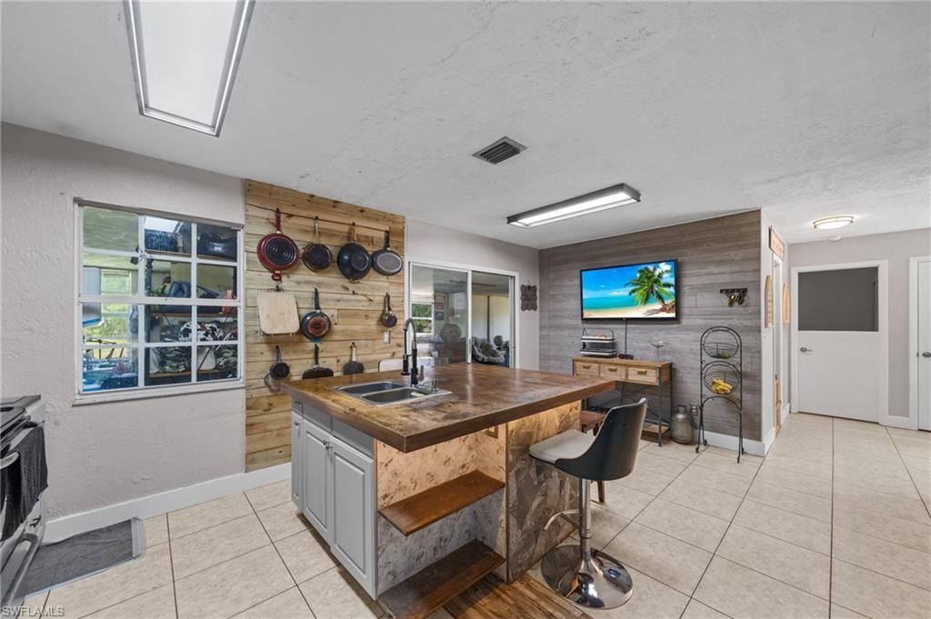 Kitchen featuring a kitchen bar, light tile patterned floors, a textured ceiling, a kitchen island with sink, and wood walls