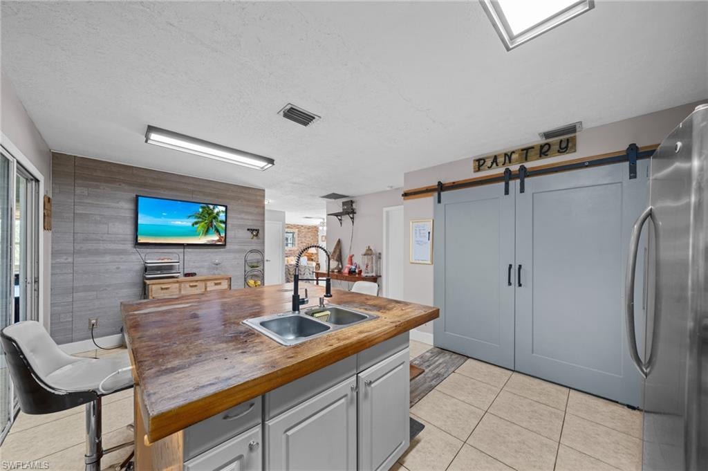 Kitchen featuring a barn door, freestanding refrigerator, wooden counters, a kitchen island with sink, and light tile patterned floors