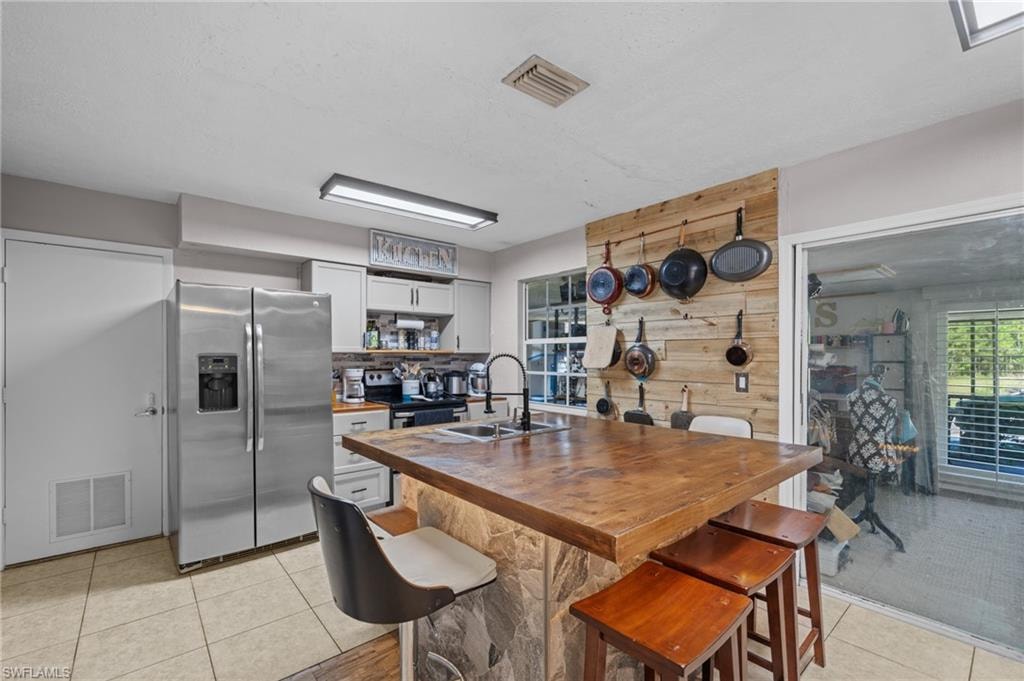 Kitchen with wooden counters, stainless steel appliances, light tile patterned flooring, a breakfast bar area, and white cabinetry