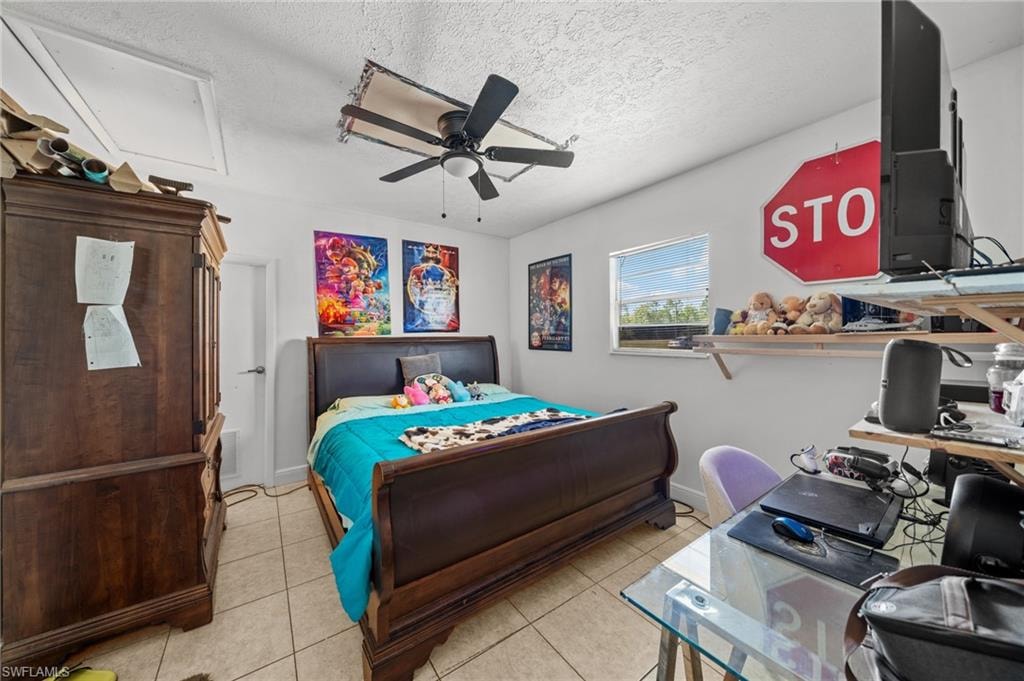 Bedroom with light tile patterned floors, a textured ceiling, a desk, a ceiling fan, and attic access