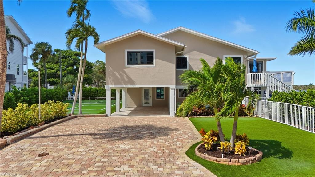 Coastal inspired home featuring stucco siding, a carport, and decorative driveway - Virtually Edited Image