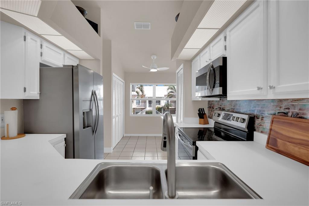 Kitchen with appliances with stainless steel finishes, light tile patterned floors, light countertops, and white cabinetry
