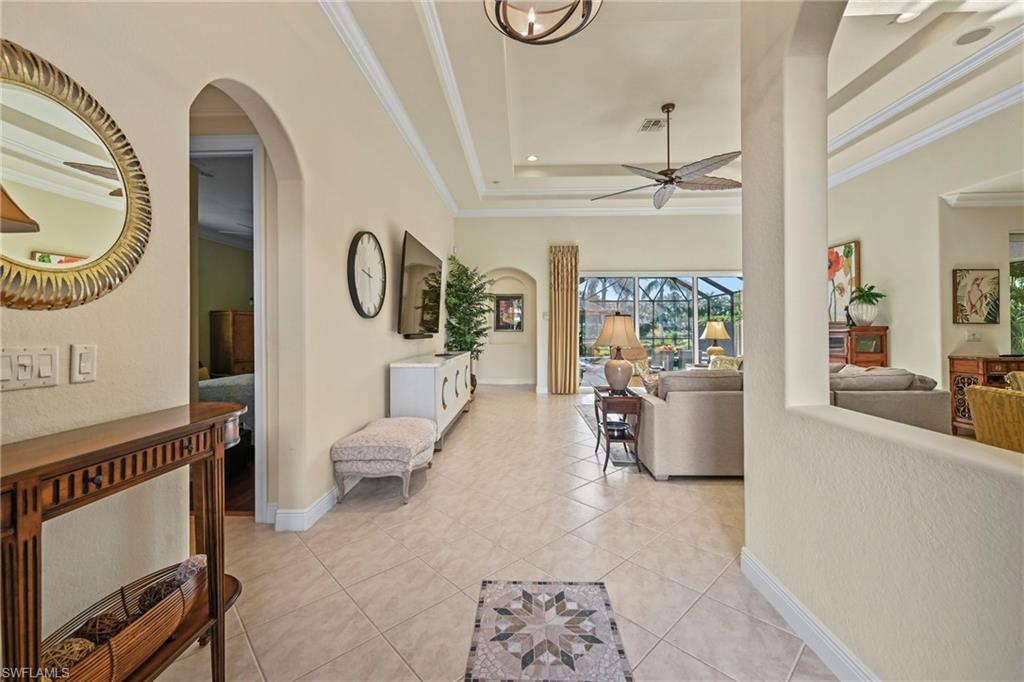 Hallway with a tray ceiling, light tile patterned flooring, arched walkways, crown molding, and a sunroom