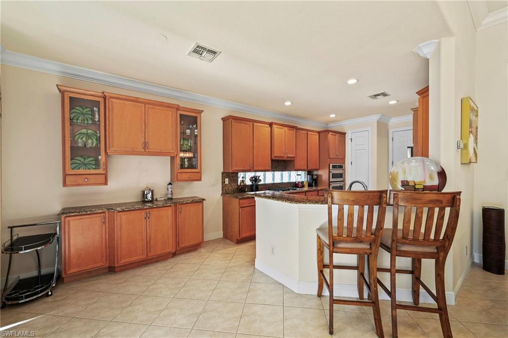 Kitchen featuring brown cabinets, a kitchen breakfast bar, ornamental molding, glass insert cabinets, and light tile patterned floors