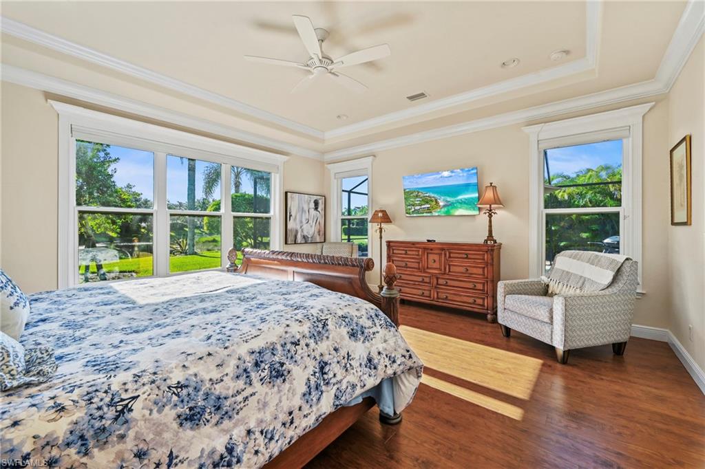 Bedroom featuring a tray ceiling, dark wood-style floors, ornamental molding, and a ceiling fan