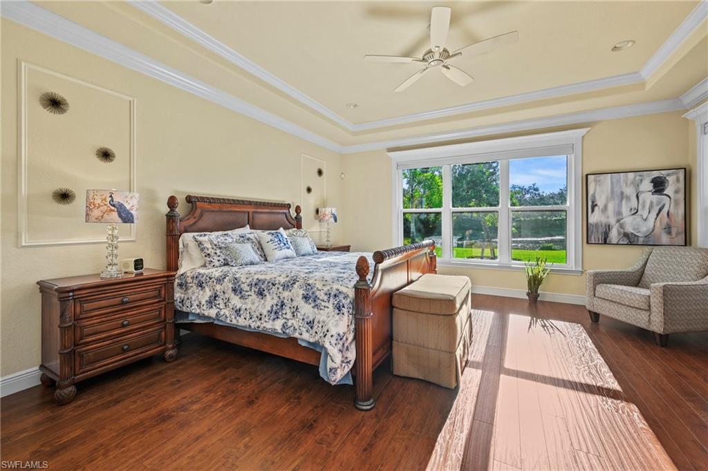 Bedroom with crown molding, dark wood-style floors, a tray ceiling, and a ceiling fan