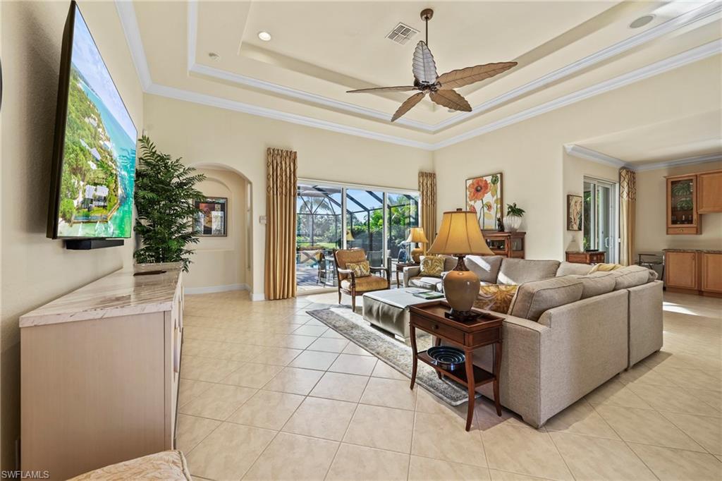 Living room featuring a tray ceiling, ornamental molding, light tile patterned floors, a sunroom, and a ceiling fan