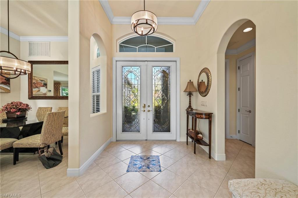 Foyer featuring crown molding, a chandelier, light tile patterned floors, arched walkways, and french doors