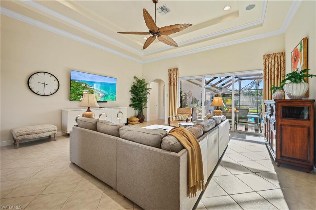 Living room with a tray ceiling, light tile patterned floors, crown molding, a ceiling fan, and a sunroom
