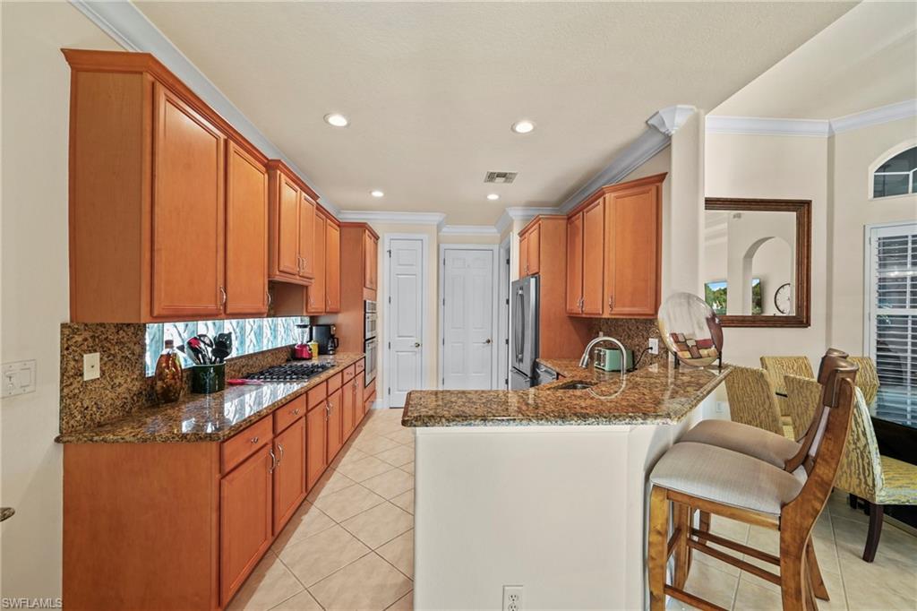Kitchen with brown cabinetry, backsplash, dark stone counters, ornamental molding, and recessed lighting