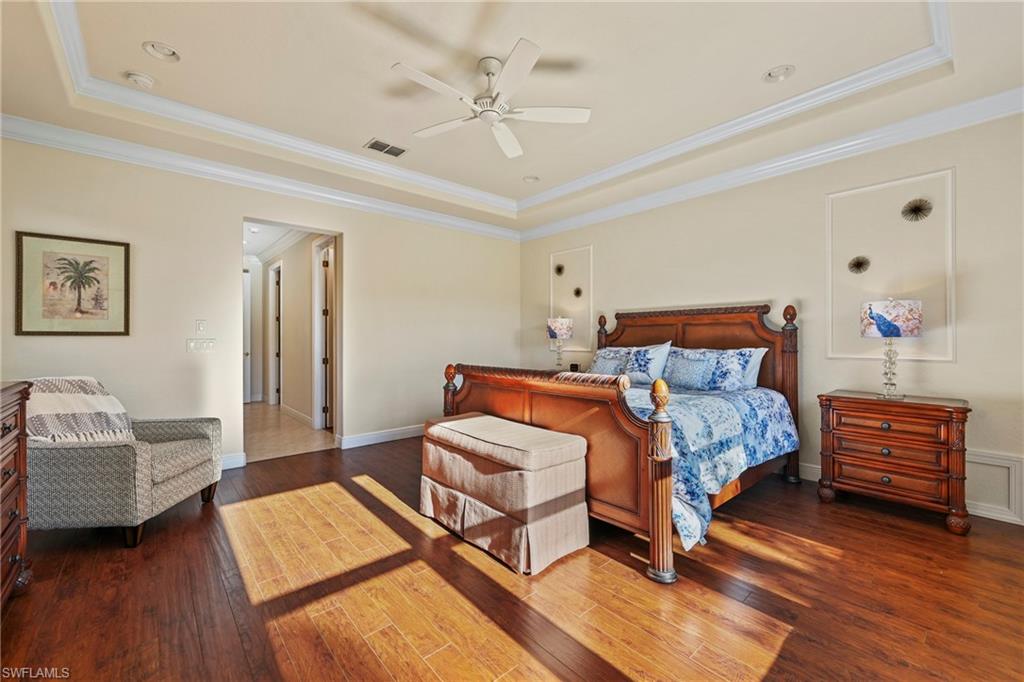 Bedroom featuring a raised ceiling, ornamental molding, dark wood-type flooring, and ceiling fan