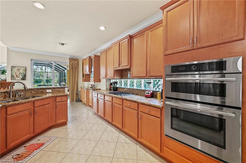 Kitchen with appliances with stainless steel finishes, crown molding, dark stone countertops, brown cabinets, and light tile patterned floors