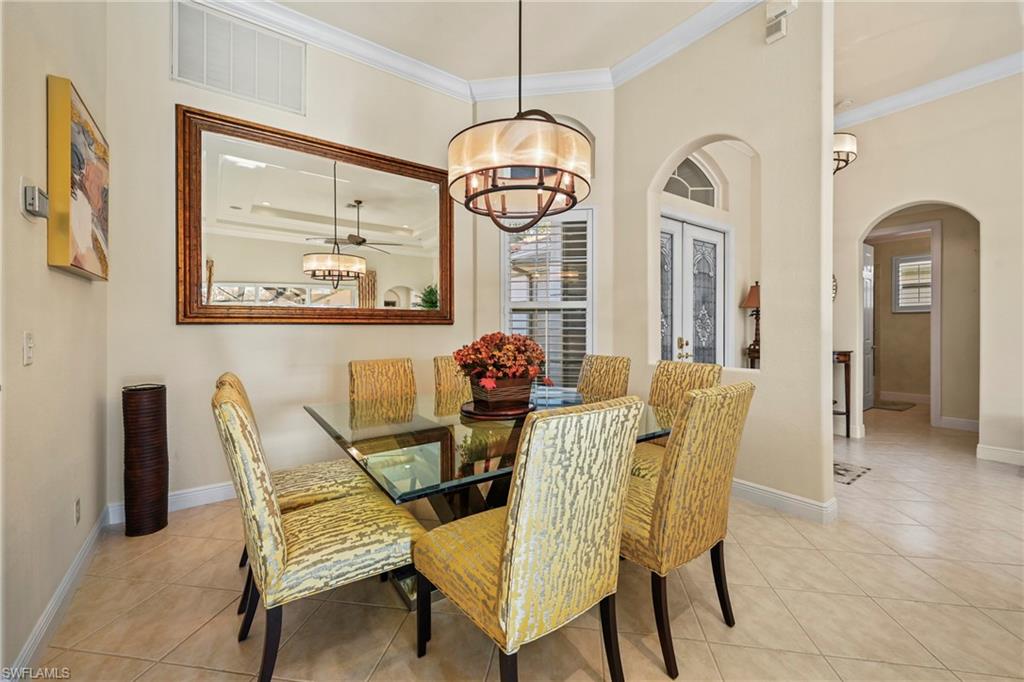 Dining room featuring ornamental molding, light tile patterned flooring, arched walkways, french doors, and a chandelier