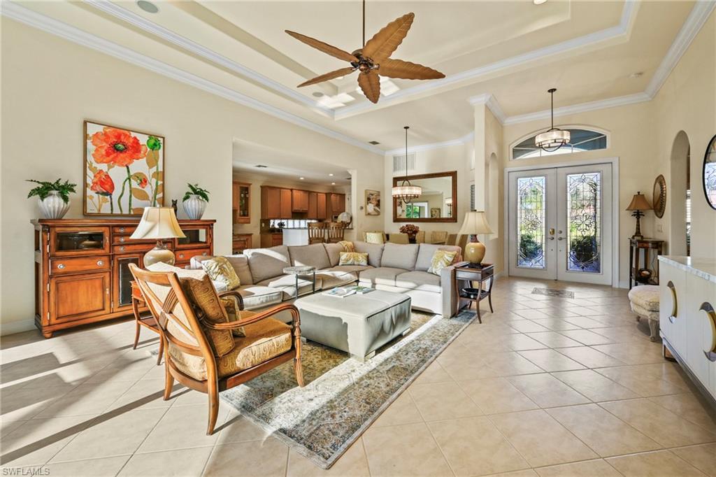Living room featuring a raised ceiling, light tile patterned floors, a high ceiling, crown molding, and french doors