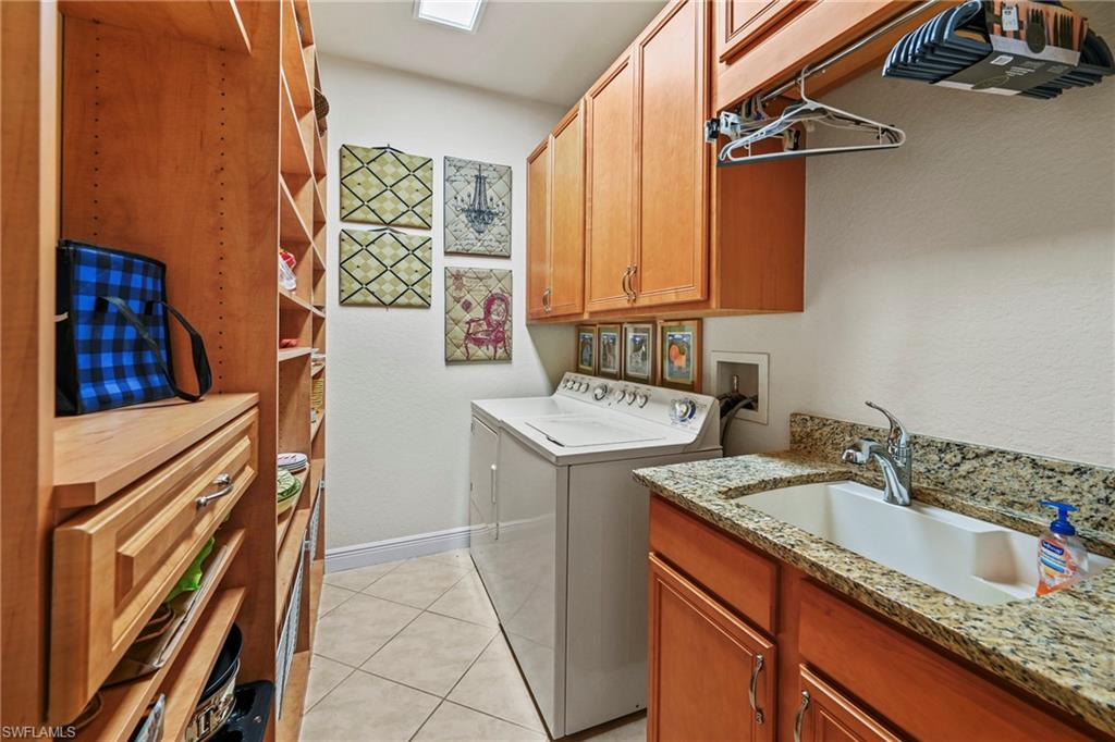 Laundry room featuring light tile patterned flooring, a textured wall, separate washer and dryer, and cabinet space