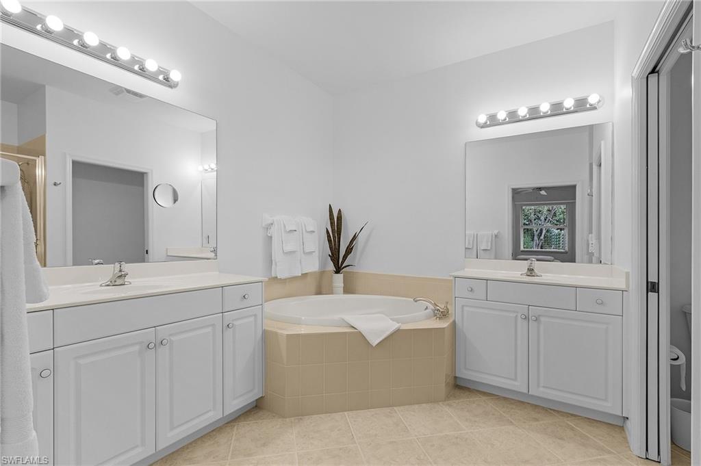 Primary en-suite bathroom featuring tile patterned floors, shower with separate bathtub, and double vanities.