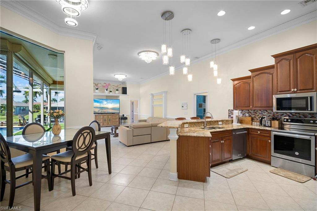 Kitchen featuring ornamental molding, hanging light fixtures, stainless steel appliances, a peninsula, and open floor plan