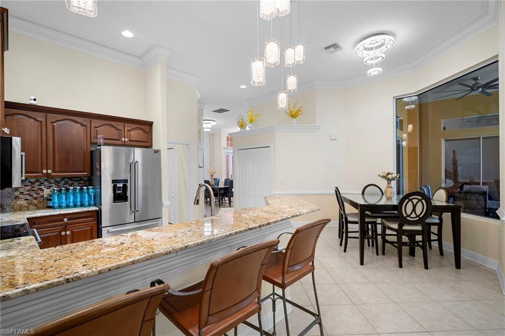 Kitchen with light stone counters, high end refrigerator, ornamental molding, hanging light fixtures, and a kitchen bar