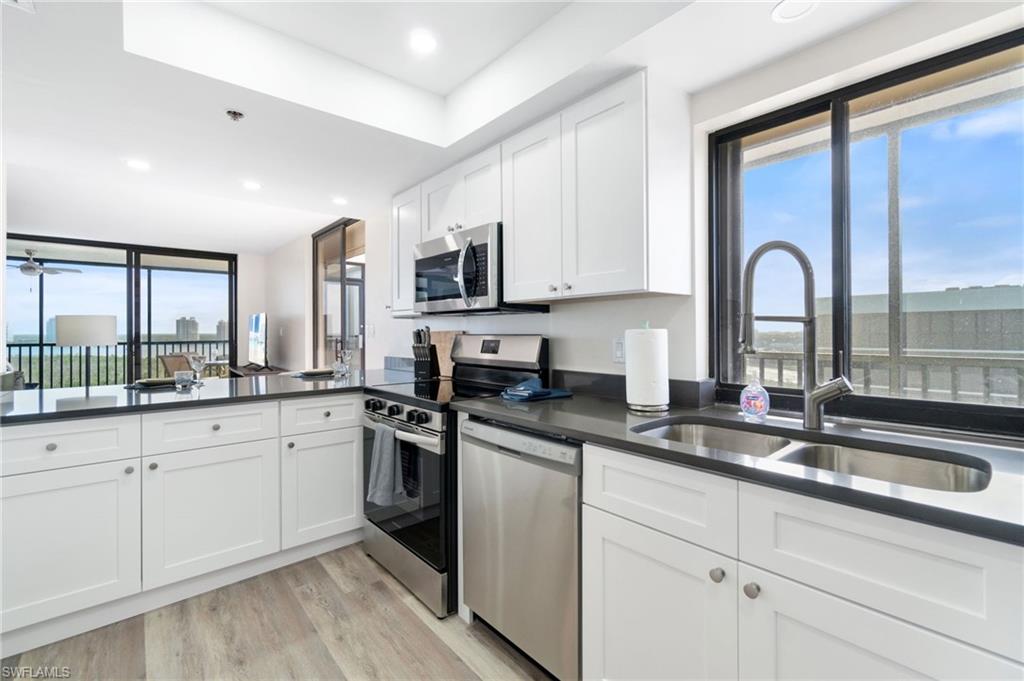 Kitchen with white cabinets, stainless steel appliances, light wood finished floors, recessed lighting, and dark stone countertops