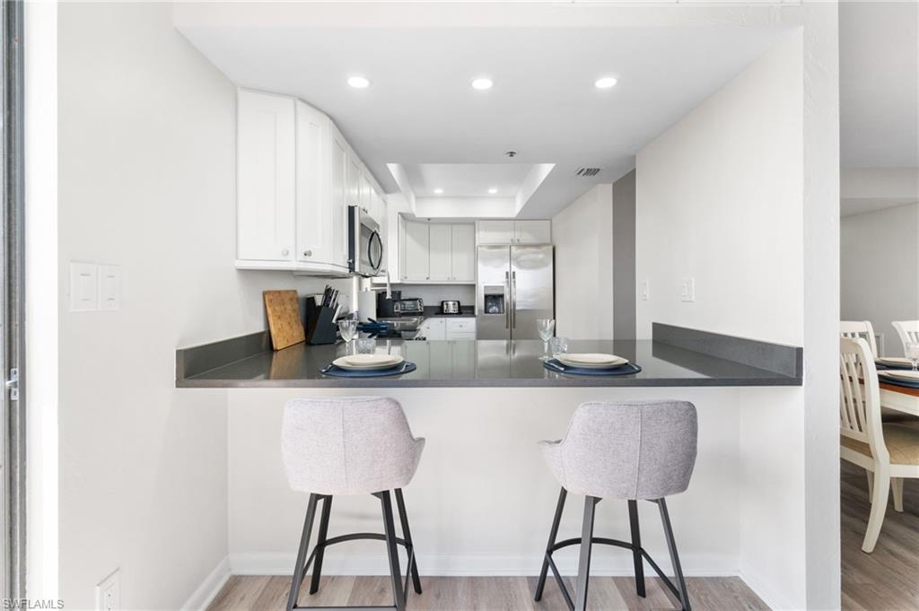 Kitchen featuring white cabinets, appliances with stainless steel finishes, a kitchen bar, light wood-type flooring, and recessed lighting