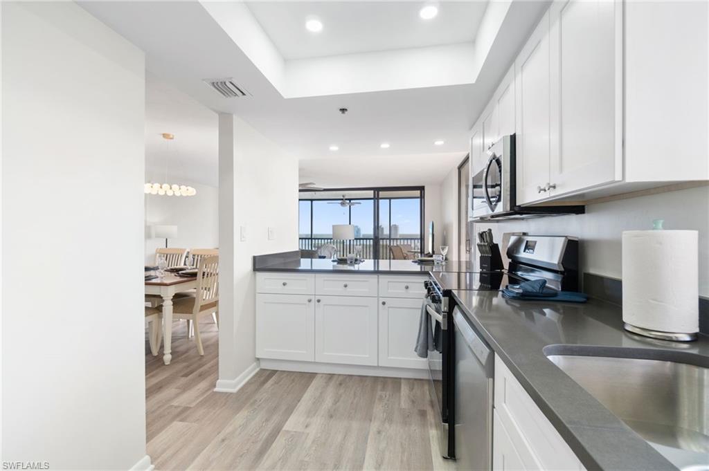 Kitchen with light wood-style flooring, stainless steel appliances, white cabinetry, a tray ceiling, and recessed lighting