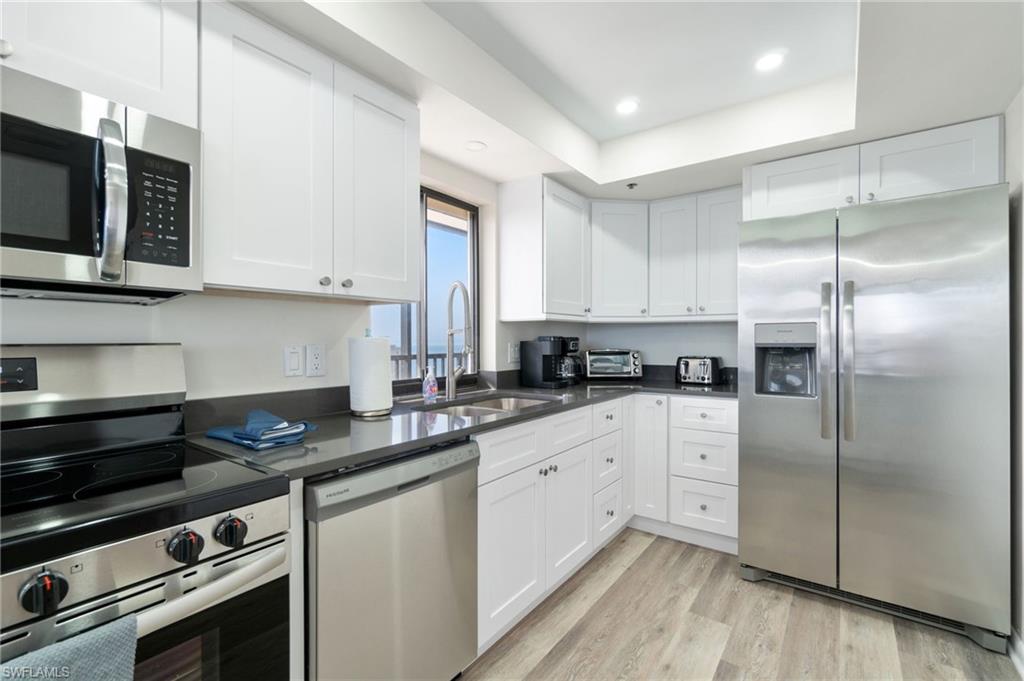 Kitchen with appliances with stainless steel finishes, white cabinetry, light wood finished floors, recessed lighting, and dark stone countertops