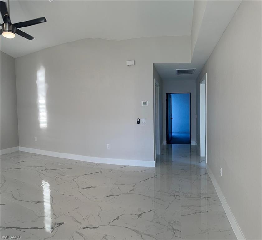 Unfurnished room featuring light marble finish flooring, ceiling fan, and vaulted ceiling