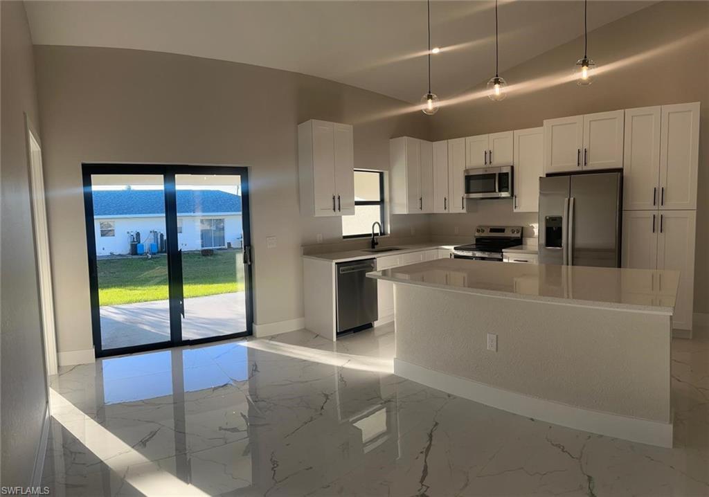 Kitchen with light marble finish floors, stainless steel appliances, white cabinets, pendant lighting, and a kitchen island