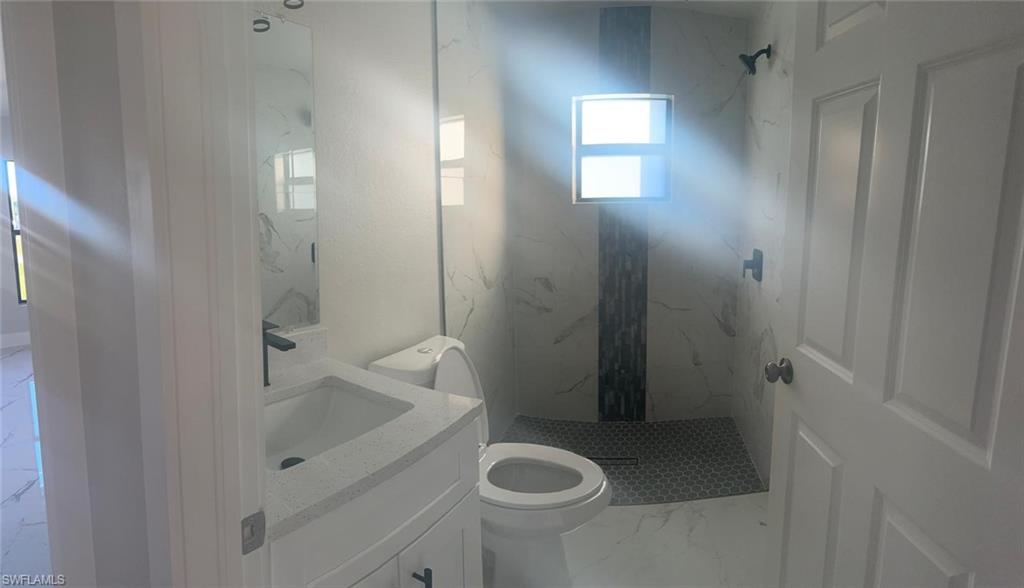 Bathroom featuring vanity, a marble finish shower, and light marble finish floors