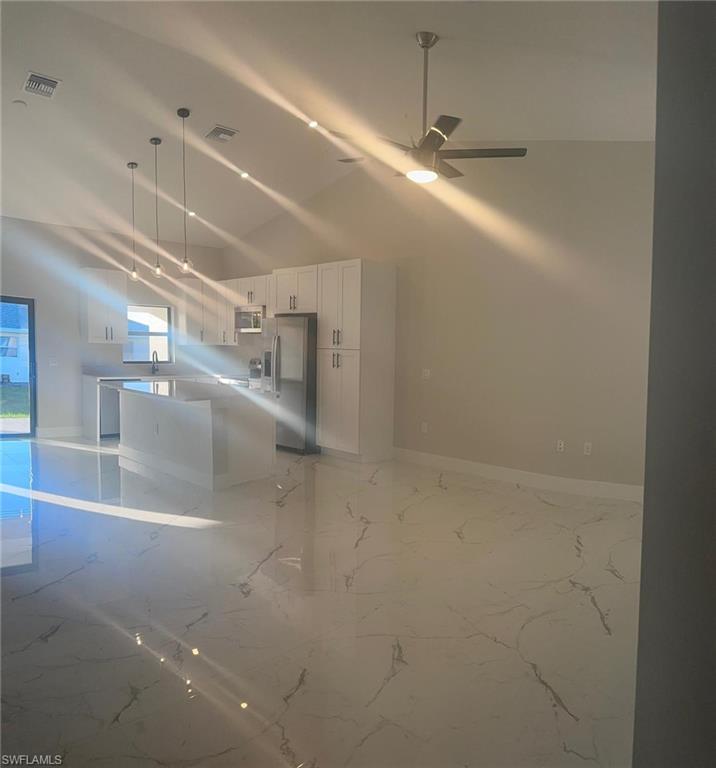 Kitchen featuring light marble finish flooring, white cabinets, appliances with stainless steel finishes, pendant lighting, and a center island