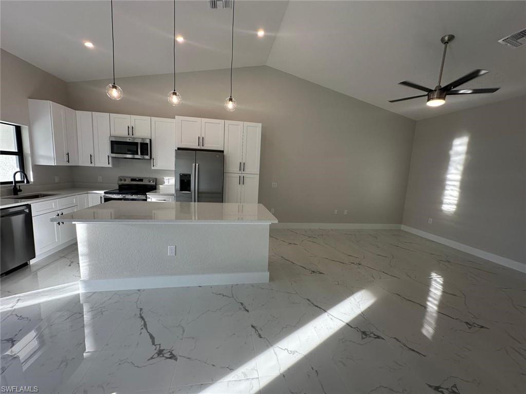 Kitchen featuring a center island, white cabinetry, appliances with stainless steel finishes, decorative light fixtures, and light stone counters