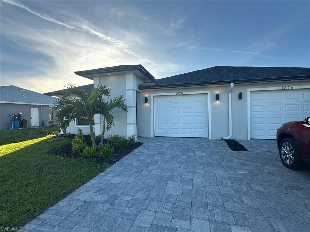 View of front of house with decorative driveway, stucco siding, a front lawn, and a garage