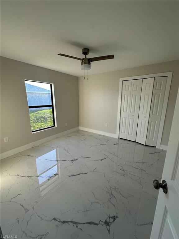 Unfurnished bedroom featuring light marble finish floors, a closet, and a ceiling fan
