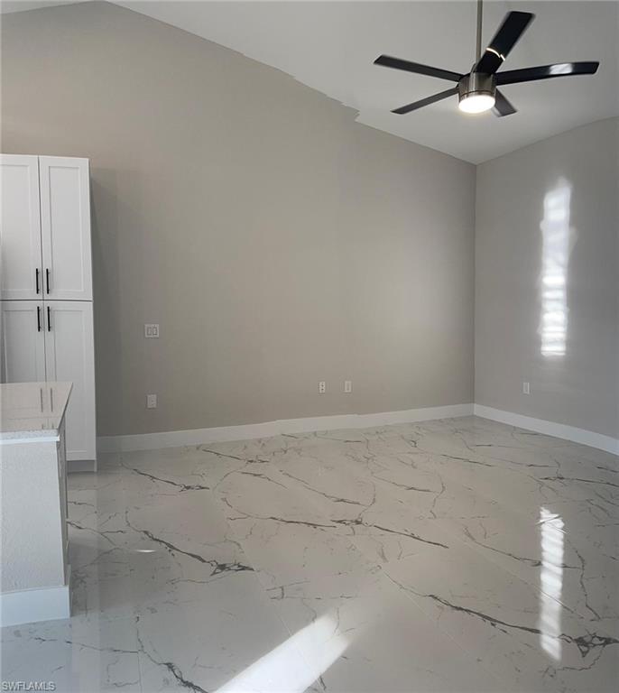 Spare room featuring light marble finish floors, ceiling fan, and vaulted ceiling