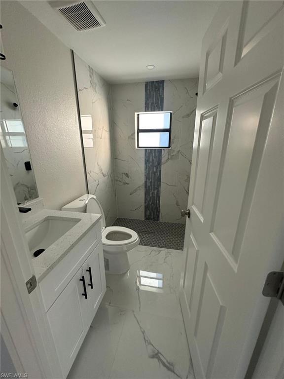 Full bath with vanity, a marble finish shower, light marble finish flooring, and a textured wall