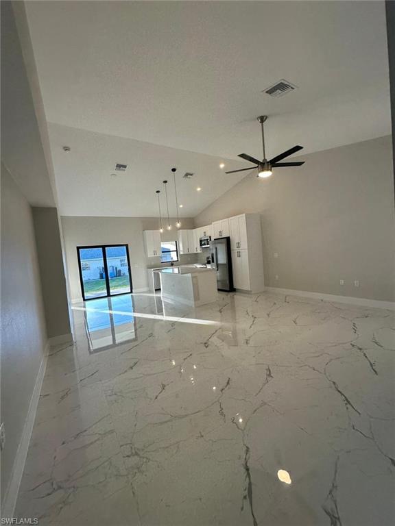 Kitchen with open floor plan, white cabinetry, hanging light fixtures, vaulted ceiling, and appliances with stainless steel finishes