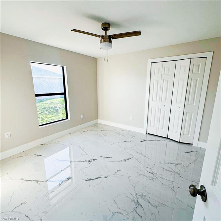 Unfurnished bedroom featuring light marble finish floors, ceiling fan, and a closet