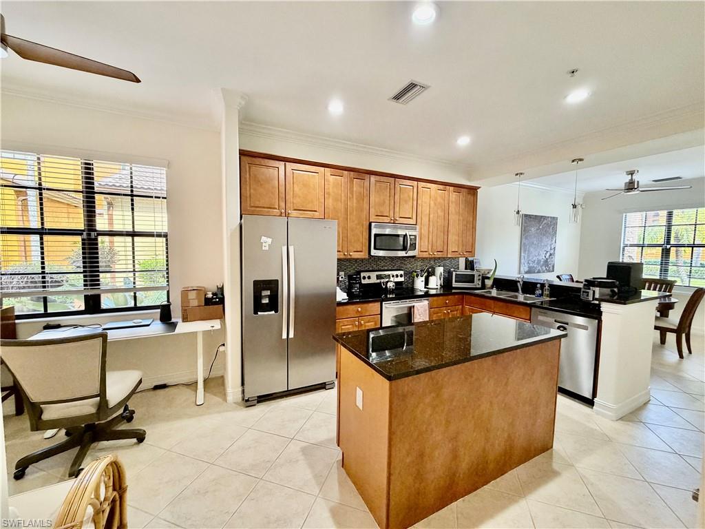 Kitchen featuring ceiling fan, stainless steel appliances, brown cabinets, crown molding, and a center island
