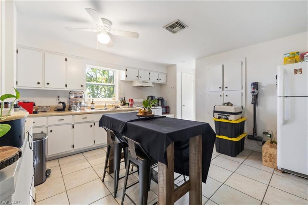 Kitchen with light tile patterned floors, freestanding refrigerator, white cabinetry, and light countertops