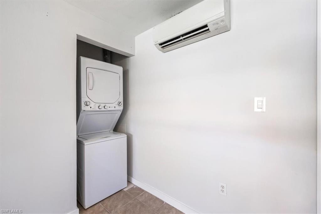 Laundry room featuring a wall mounted AC, light tile patterned floors, and stacked washer / drying machine