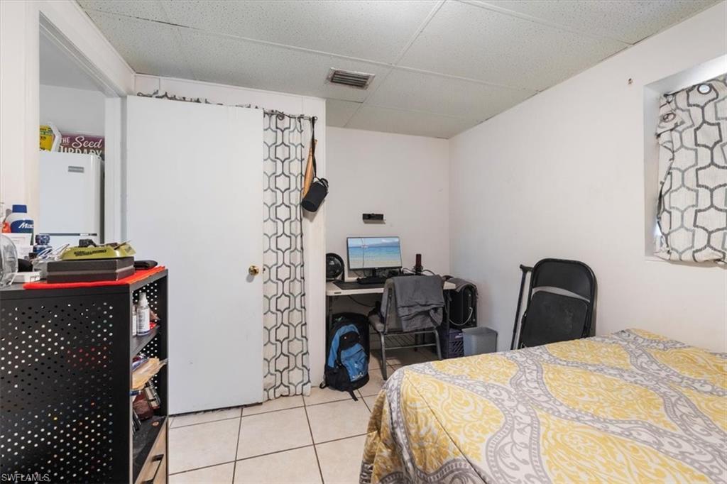 Bedroom featuring an office area, a paneled ceiling, light tile patterned floors, and freestanding refrigerator