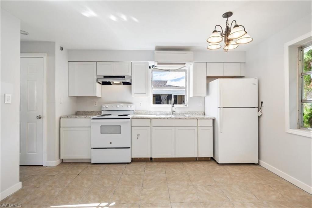 Kitchen with white appliances, white cabinetry, under cabinet range hood, decorative light fixtures, and light tile patterned floors