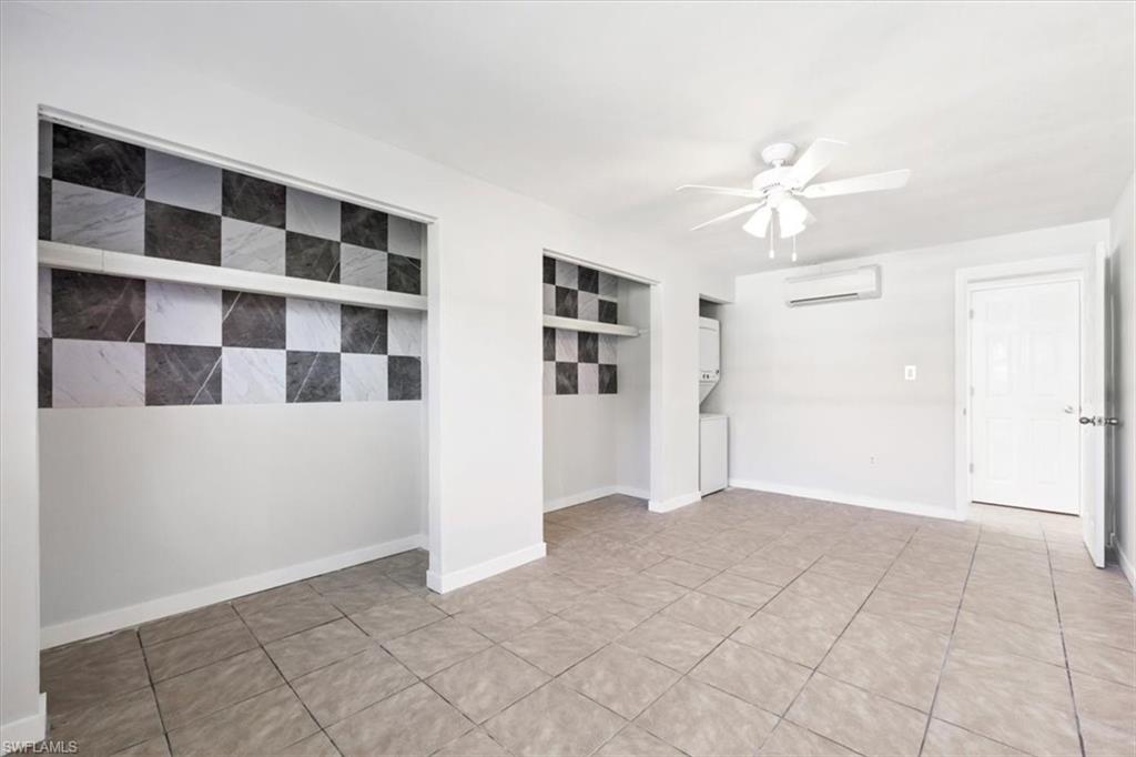 Unfurnished room with estacked washer and dryer, a wall mounted air conditioner, light tile patterned floors, and a ceiling fan