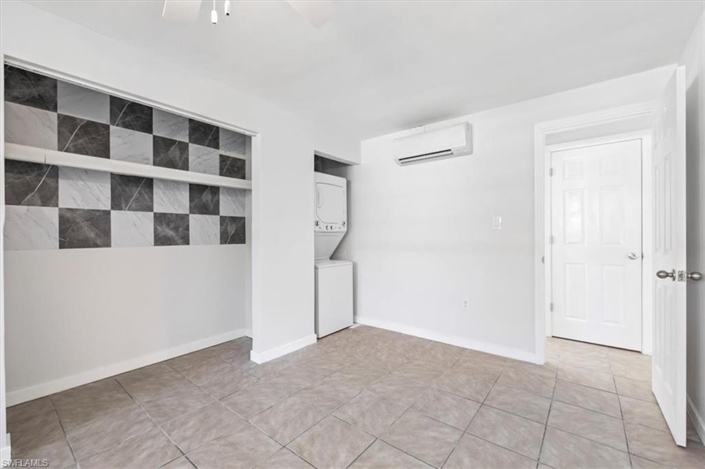 Unfurnished room featuring stacked washer and clothes dryer, a wall mounted AC, light tile patterned floors, and a ceiling fan