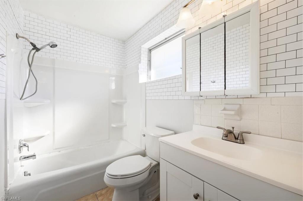 Full bathroom featuring shower / bathtub combination, tile walls, vanity, tasteful backsplash, and light tile patterned floors