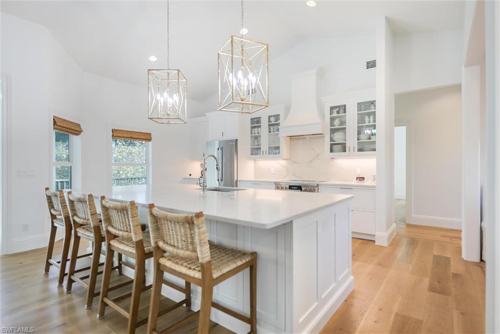 Kitchen with premium range hood, white cabinetry, sink, hanging light fixtures, and a large island with sink