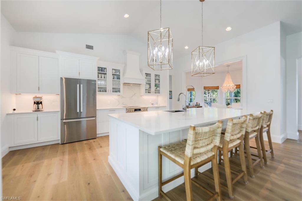 Kitchen with white cabinetry, sink, stainless steel fridge, custom exhaust hood, and a spacious island